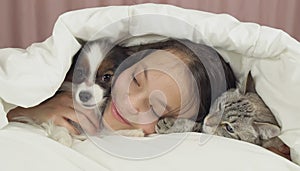 Happy teen girl communicates with dog Papillon and Thai cat in bed