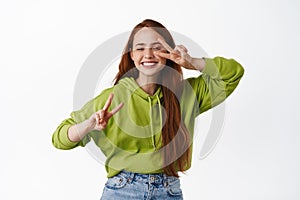 Happy teen girl dancing with v-signs peace, show kawaii gesture, laughing and smiling white teeth, standing in casual