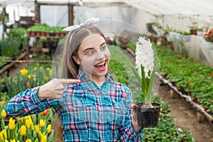 happy teen girl florist in greenhouse. spring and summer. pointing finger on pot plants.