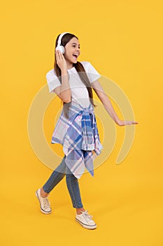 Happy teen girl in headphones singing along to song yellow background, music