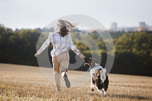 Happy teen girl with her dog running across field