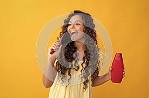 happy teen girl with long curly hair hold shampoo bottle singing in hairbrush, fun