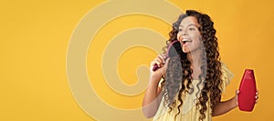 happy teen girl with long curly hair hold shampoo bottle singing in hairbrush, fun. Banner of child girl hair care