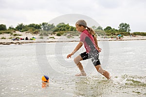 Happy teen girl in neoprene swimingsuit  playing with ball and running in sea