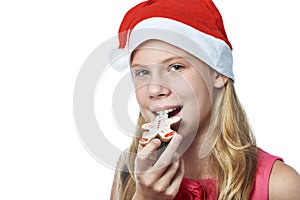 Happy teen girl in red cap eating Christmas cookie isolated