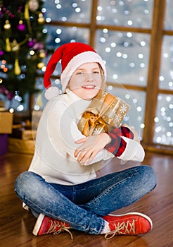 Happy teen girl in red christmas hat hugging christmas gift box