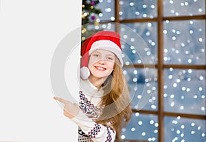 Happy teen girl in red christmas hat peeking and pointing at empty board