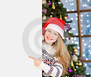 Happy teen girl in red christmas hat peeking and pointing at empty board