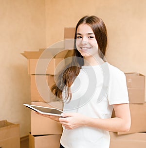 Happy teen girl with tablet computer standing on a background of boxes