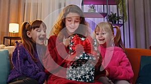 Three siblings children girls opening gift box with excited surprised face, birthday glowing present