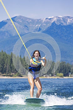 Happy teen girl wake boarding at a picturesque mountain lake on her summer vacation. Boating lifestyle