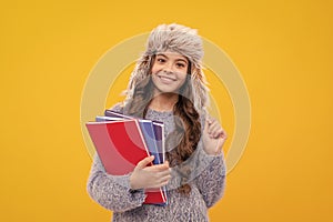 happy teen girl wear earflap hat with notebook on yellow background, education