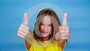 Happy teen girl in a yellow t-shirt is smiles, showing thumbs up, like and looking at camera