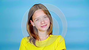 Happy teen girl in a yellow t-shirt is straightens hair with one hand, smiling, posing and looking at the camera