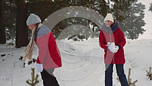 Happy teen girls play snowballs in snowy winter and laugh with pleasure. Walking in fresh air of children in pine park