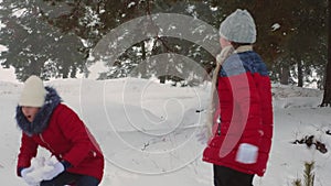 Happy teen girls play snowballs in snowy winter and laugh with pleasure. Walking in fresh air of children in pine park