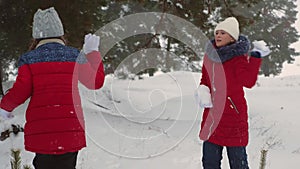 Happy teen girls play snowballs in snowy winter and laugh with pleasure. Walking in fresh air of children in pine park