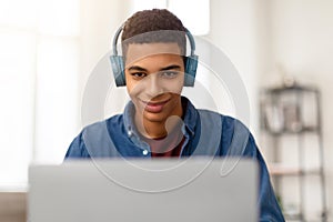 Happy teen guy with headphones using laptop and smiling