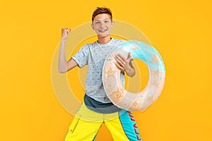 Happy teen guy, standing with an inflatable sea circle and celebrating victory, isolated on a yellow background