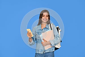 Happy teen Latin girl student holding backpack using phone isolated on blue.