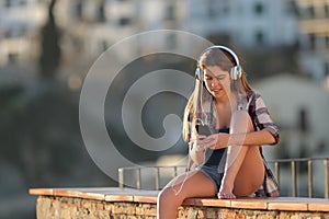 Happy teen listening to music from smart phone on a ledge