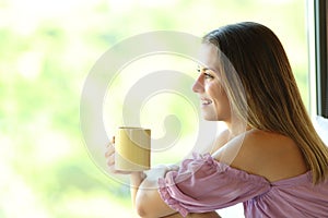 Happy teen looking through a window holding coffee mug