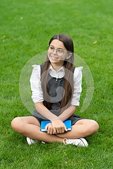 Happy teen school girl sitting legs crossed on grass. School and education. Back to school
