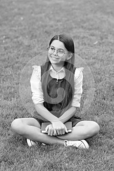 Happy teen school girl sitting legs crossed on grass. School and education. Back to school