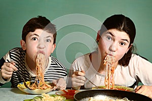 Happy teen siblings boy and girl eat spaghetti