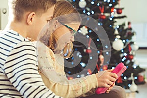 Happy teen siblings children or friends playing games with tablet on sofa near christmas tree at home