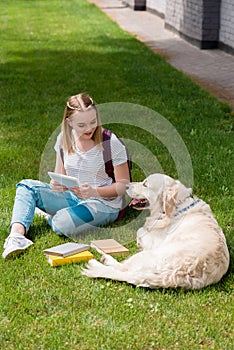 happy teen student girl using tablet while sitting on grass