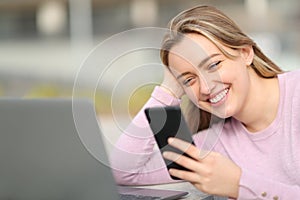 Happy teen using phone and laptop in the street