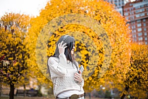 Happy teen woman listening to music and relax in autumn park. Yellow trees, beautiful fall time