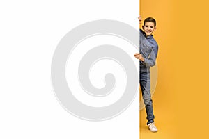 Happy teenage boy peeking and smiling from behind blank white banner