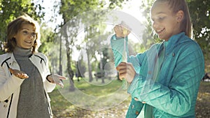 Happy teenage caucasian girl playing with soap bubbles in the sunny park. Granddaughter entertaining her young-looking