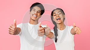 Happy teenage couple showing thumbs up over pink background