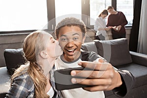 Happy teenage couple taking selfie with friends standing behind