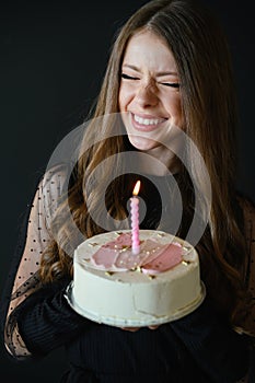 Happy teenage girl with birthday cake laughing, keeping eyes closed