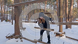 Happy teenage girl climb on swinging suspended wooden logs in winter adventure park in snowy forest. Winter fun and