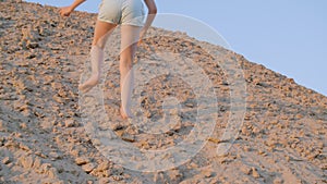 Happy teenage girl climbing on sand dune in desert