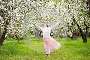 Happy teenage girl dancing in blooming garden with blossom flowers on apple trees