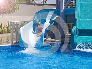 Happy teenage girl going down by water slide into the pool