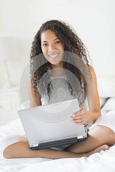 Happy Teenage Girl With Laptop Sitting On Bed