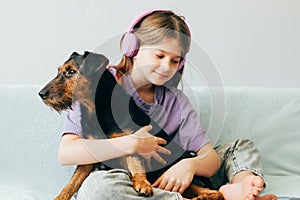 Happy teenage girl in lilac t-shirt in pink headphones listens to music and has fun playing with dog