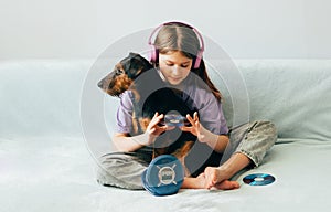 Happy teenage girl in lilac t-shirt in pink headphones listens to music and has fun playing with dog