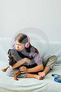 Happy teenage girl in lilac t-shirt in pink headphones listens to music and has fun playing with dog