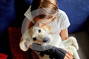 Happy teenage girl lying on sofa and embracing her puppy golden retriever