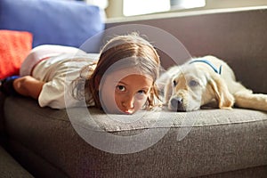 Happy teenage girl lying on sofa and embracing her puppy golden retriever