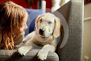 Happy teenage girl lying on sofa and embracing her puppy golden retriever