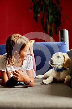 Happy teenage girl lying on sofa and embracing her puppy golden retriever